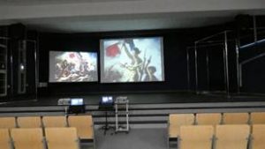 Aula dla Kultury w Zespole Szkół Nr 1 przy ulicy Słubickiej widok sceny z dwoma ekranami – na nich obraz Eugèna Delacroix „Wolność wiodąca lud na barykady”